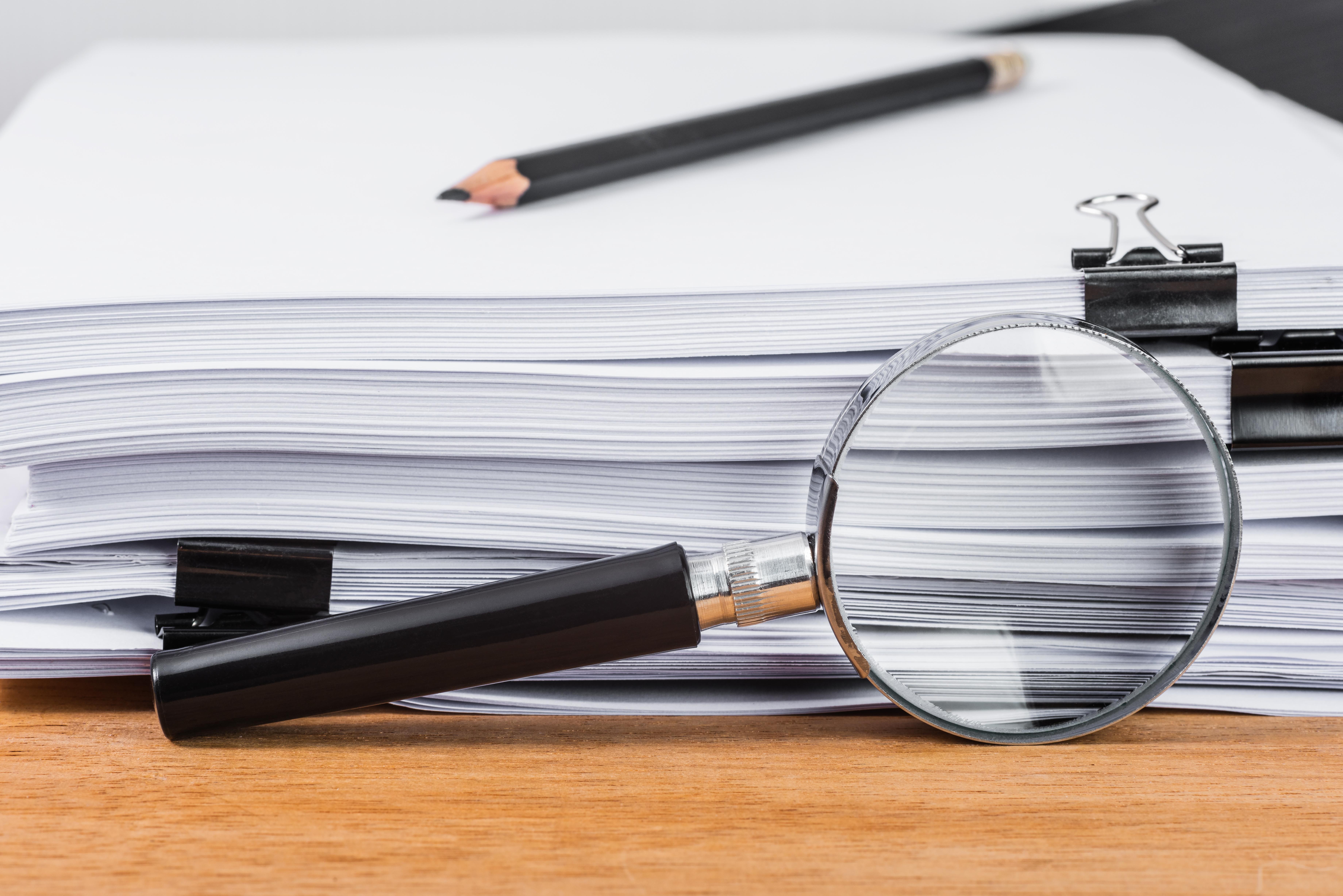 Magnifying glass agains stacks of paper